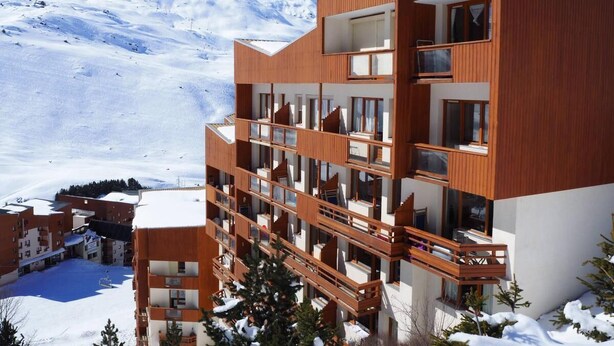 Ein mehrstöckiges Hotel mit hölzernen Balkonen vor einer verschneiten Bergkulisse.