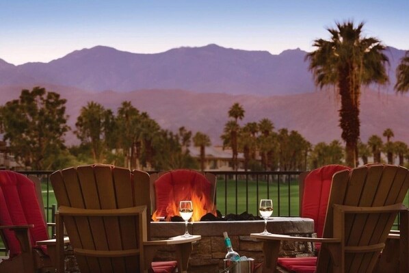 Un patio con sillas de madera, una mesa de piedra y una chimenea.