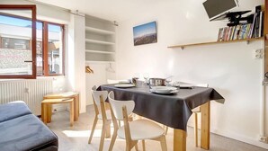 Un coin repas avec une table dressée pour quatre personnes, une nappe noire et une bibliothèque contenant des livres et un téléviseur.