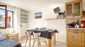 Un coin repas avec une table dressée pour quatre personnes, des chaises en bois, une nappe noire et une vue sur la ville par la fenêtre.