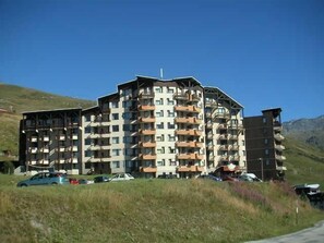 Un hôtel à plusieurs étages doté de balcons, situé dans une zone vallonnée où le ciel est dégagé.