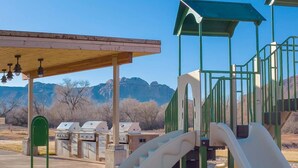 A playground with slides and climbing structures, barbecue grills, and a covered seating area with a view of mountains. - Worldmark Moab 2 Bedroom Condo (Moab)