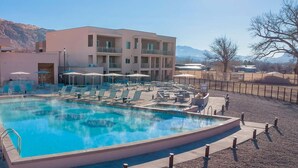 A pool area with lounge chairs and umbrellas, a large pool, and a building with multiple balconies. - Worldmark Moab 2 Bedroom Condo (Moab)