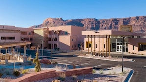 A modern building with a covered outdoor area, a parking lot, and a mountainous backdrop. - Worldmark Moab 2 Bedroom Condo (Moab)