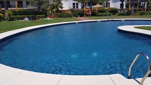A large, clear blue swimming pool with a curved edge, surrounded by a paved deck.