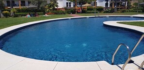 A large, clear blue swimming pool with a curved edge, surrounded by a paved deck.
