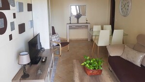 Uma sala de estar com sofá, televisão e área de refeições com cadeiras e mesa.