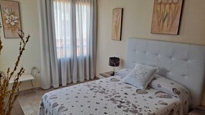 A bedroom with a bed, a nightstand, a lamp, and a window with curtains.