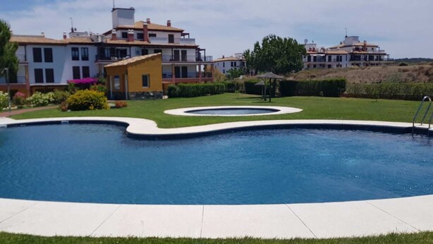 A swimming pool with a curved edge, surrounded by a well-maintained lawn and a building with multiple balconies.