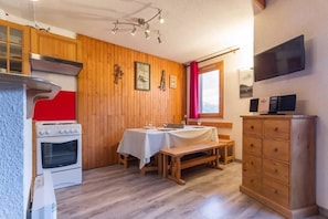 Una cucina con pareti in legno, un fornello bianco, un tavolo da pranzo con panche e una TV a muro.