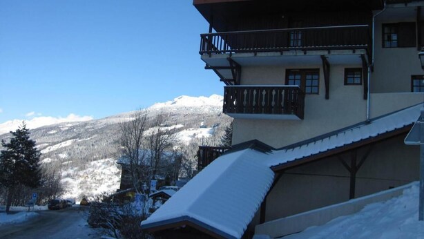 Un bâtiment enneigé doté d’un balcon, offrant une vue sur les montagnes et surplombant un ciel dégagé.