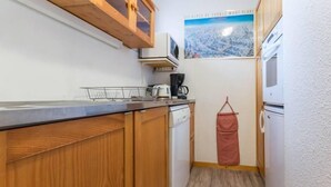 Une cuisine compacte avec des meubles en bois, un lave-vaisselle, une machine à café et une petite poubelle.