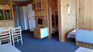 Eine Holzhütte mit einem Etagenbett, einem Schreibtisch mit Computer, einem Stuhl und einem Kühlschrank.