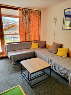 Ein Zimmer mit einer Couch, einem kleinen Tisch und Blick auf ein Gebäude durch ein Fenster.