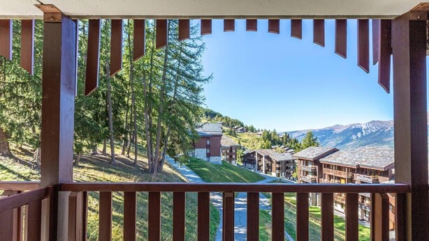 Un balcon en bois offrant une vue sur un paysage montagneux, un bâtiment doté d’un toit en pente et un ciel dégagé.