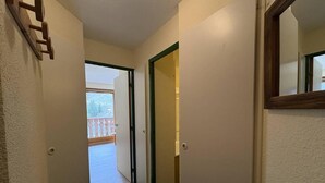 A narrow hallway with a wooden door on the left, a green carpet, and a view of a balcony with a railing. - 300m from resort center, 3rd floor, view mountain, balcony, 27m², Méribel-Mottaret (Méribel - Les Allues)