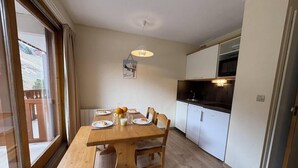 A dining area with a wooden table set for four, a bench, and a kitchen with white cabinets and a black countertop. - 300m from resort center, 3rd floor, view mountain, balcony, 27m², Méribel-Mottaret (Méribel - Les Allues)