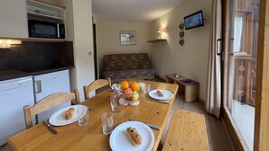 A dining area with a wooden table set for two, a microwave, a small refrigerator, and a sofa in the background. - 300m from resort center, 3rd floor, view mountain, balcony, 27m², Méribel-Mottaret (Méribel - Les Allues)