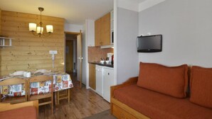 Una habitación acogedora con una mesa de comedor de madera, un sofá, un televisor montado en la pared y una zona de cocina.