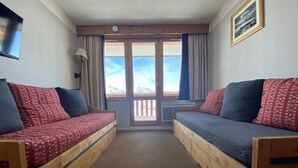 Una habitación con dos literas de madera, ropa de cama roja y azul, un ventanal con vistas y un cuadro en la pared.