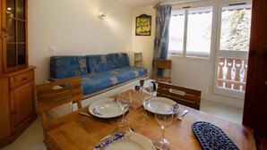 A dining area with a wooden table set for two, a blue sofa, and a window with a view of trees. - 70m from ski slopes, 3rd floor, view mountain, parking, tv, ski locker, 20m², Valfréjus (Valfréjus)