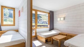 A room with two wooden beds, a small wooden table, and a window with a view of a house and trees. - 50m from ski slopes, 5th floor, balcony, tv, 28m², Montchavin La Plagne (Bellentre)
