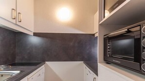 A compact kitchen with a black microwave, white cabinets, and a black countertop. - 50m from ski slopes, 5th floor, balcony, tv, 28m², Montchavin La Plagne (Bellentre)