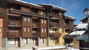 A multi-story wooden building with balconies, a stone base, and a snow-covered ground. - 50m from ski slopes, 5th floor, balcony, tv, 28m², Montchavin La Plagne (Bellentre)