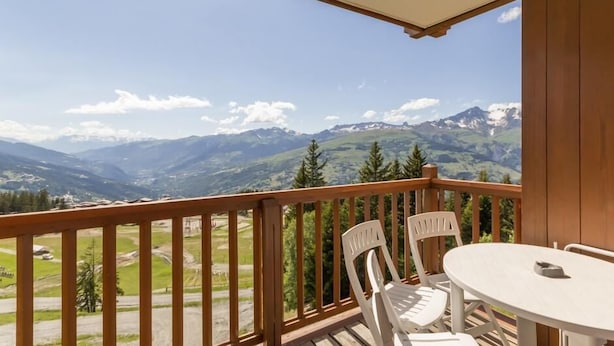 Un balcon doté d’une balustrade en bois, de deux chaises blanches et d’une table ronde.