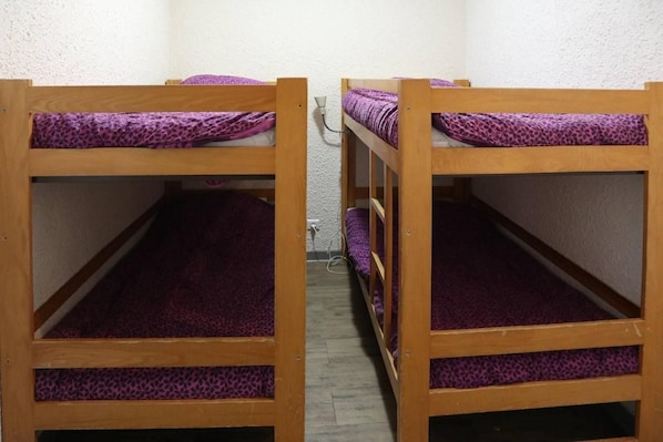 Two wooden bunk beds with purple bedding in a room with white walls.