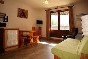 A room with a bed, a desk, a chair, a television, and a window with curtains.
