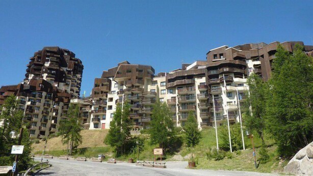 En grupp moderna bostadshus med flera våningar och balkonger, omgivna av grönska och en klar himmel.