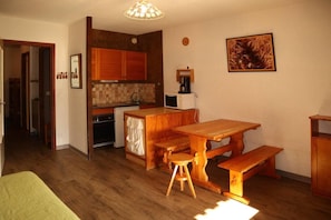 A compact kitchen with wooden cabinets, a dining table with benches, and a small refrigerator.