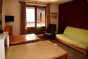 A room with a wooden table, a green sofa, a chair, and a television.