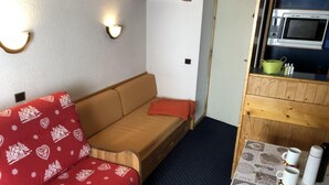 Ett litet rum med en soffa, ett litet bord med koppar och en termos, och en mikrovågsugn ovanför bordet.