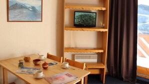 Ett rum med ett träbord dukat för frukost, en tv på en hylla och ett fönster med gardiner.