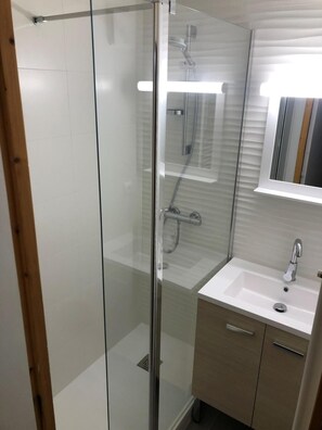 A modern bathroom with a glass shower enclosure, a white sink with a mirror above it, and wooden cabinets.