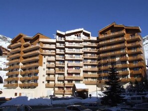 Ein mehrstöckiges Hotel mit Balkonen vor einer verschneiten Berglandschaft.