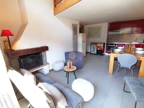 A modern living room with a fireplace, a dining area with a table and chairs, and a kitchen with appliances.