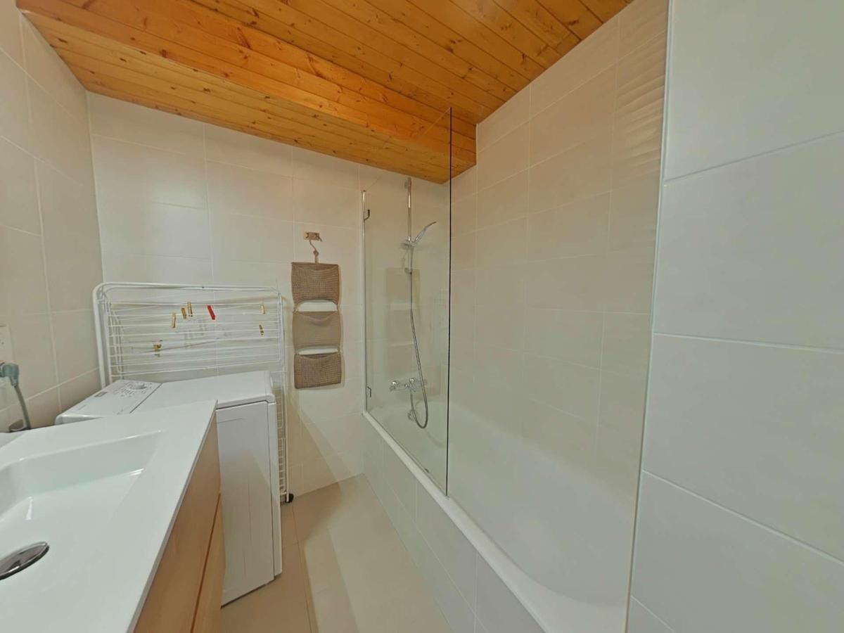 A bathroom with a wooden ceiling, white tiles, a bathtub, a shower, and a drying rack with towels.