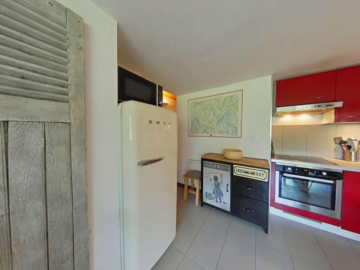 Une cuisine compacte avec un réfrigérateur blanc, une petite table en bois, un meuble rouge et une carte accrochée au mur.