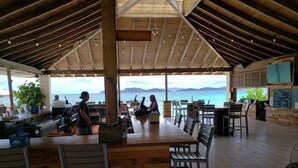 Un espace de restauration extérieur abrité, avec des tables et des chaises en bois, un comptoir de bar et une vue sur la mer.
