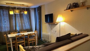 Ett kompakt vardagsrum med en soffa, ett matbord, stolar, en tv och en lampa.