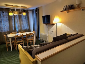 Ein gemütlicher Wohnbereich mit Sofa, Esstisch, Stühlen, Fernseher und Lampe.