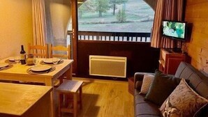 A cozy room with a dining table set for two, a sofa with cushions, a television, and a window with a view of trees. - 50m from ski lifts, 2nd floor, balcony, parking, tv, 28m², Montgenèvre (Montgenèvre)