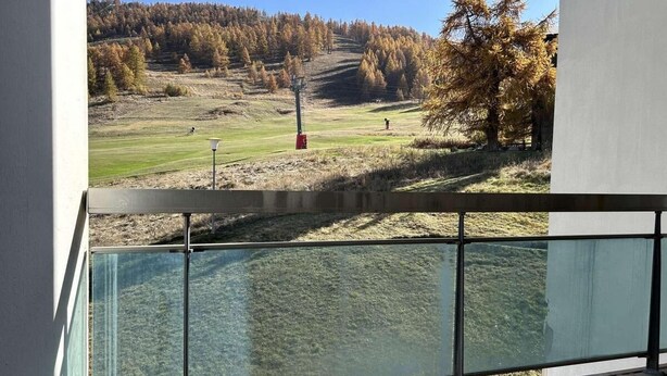A balcony with a glass railing overlooking a grassy area with trees and a distant hill. - Ski-in/ski-out & foot of the slopes, 1st floor, view ski slopes, parking, tv, 50m², Montgenèvre (Montgenèvre)