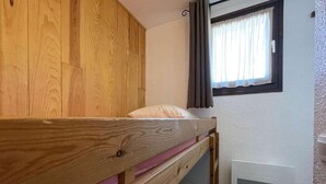 Een stapelbed met een houten hoofdeinde, een raam met gordijnen en een witte luchtuitlaat op de muur.