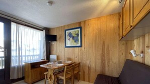 Een compacte kamer met een houten eettafel en stoelen, een bank en een schilderij aan de muur.
