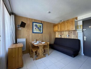 Una cucina compatta con mobili in legno, un tavolo da pranzo con sedie, un divano nero e un piccolo piano di lavoro.