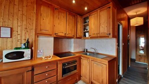 A kitchen with wooden cabinets, a microwave, a sink, and a stove. - 1st floor, view mountain, tv, 50m², Montgenèvre (Montgenèvre)